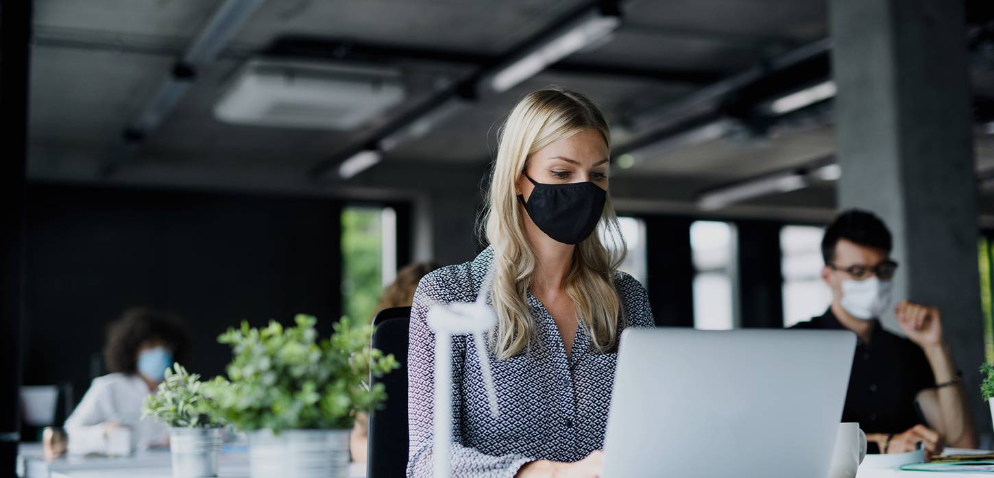 woman working at a desk wearing a face mask.